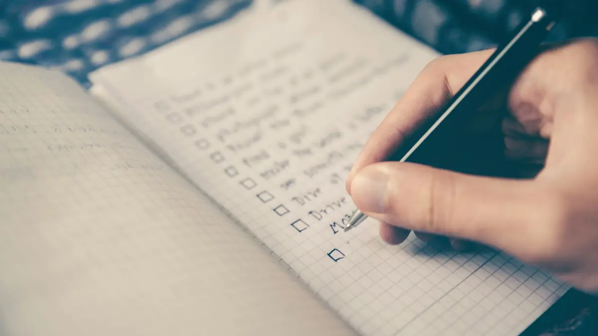 Mão marcando itens de uma lista em um caderno quadriculado