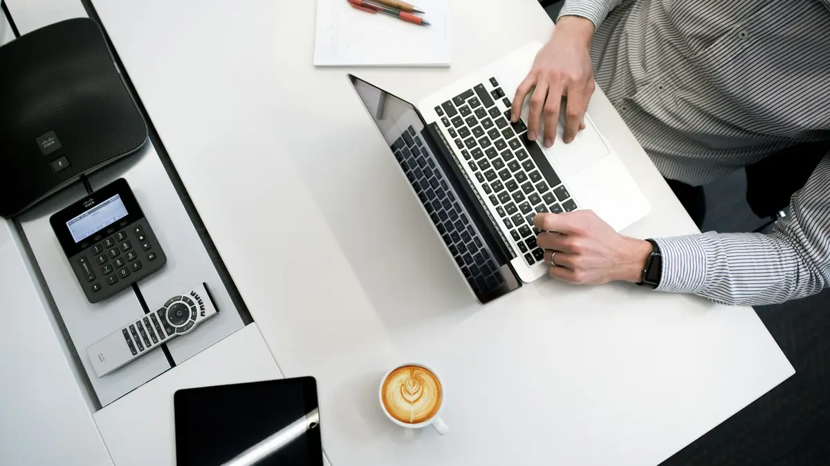 Mesa branca vista de cima com notebook, máquina de cartão e café