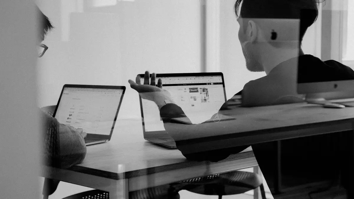 Pessoa trabalhando com dois notebooks em uma mesa, em preto e branco